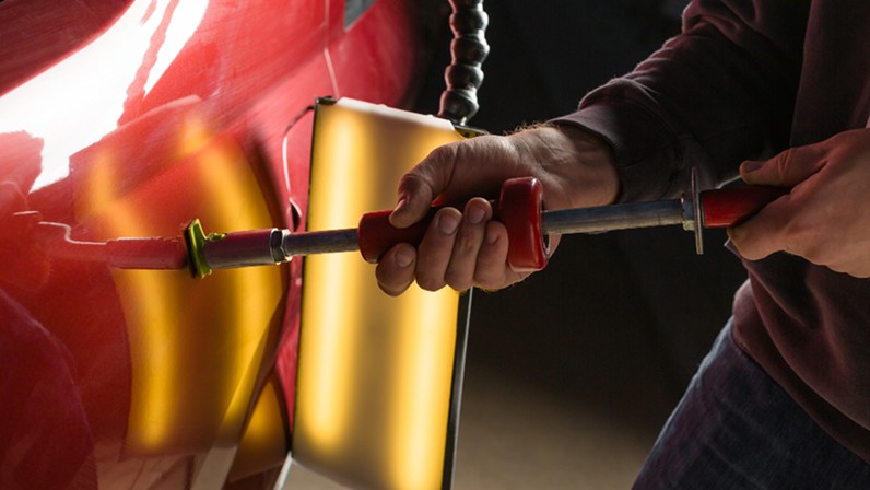 Experienced panel beaters inspecting hidden structural damage after a car collision