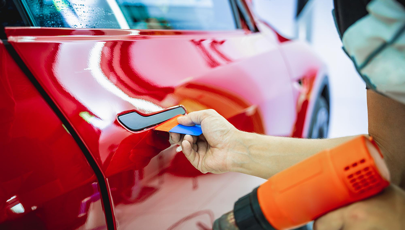 Close-up of a technician refinishing a red car door panel in a smash repair workshop in Cheltenham